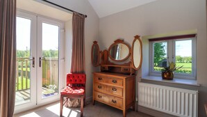 Una habitación con puerta de vidrio corredera, un sillón tapizado rojo, un aparador de madera con cajones, un espejo y una ventana con vistas a follaje.