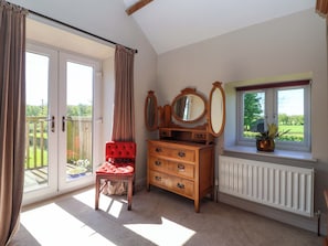 A room with a sliding glass door, a red upholstered chair, a wooden dresser with drawers, a mirror, and a window with a view of greenery. - The Granary (York)