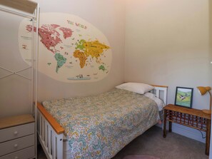 A child's bedroom with a bed, a dresser, a wall map, and a small table with a lamp. - The Granary (York)