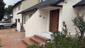 A two-story house with a tiled roof, a front door, and a small porch area. - Crest Premiums Sandton (Johannesburg)