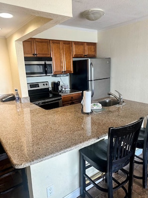 A kitchen with granite countertops, wooden cabinets, a stainless steel refrigerator, and a built-in oven. - Wake Up to Stunning Views – Your Balcony Escape! (Tampa)