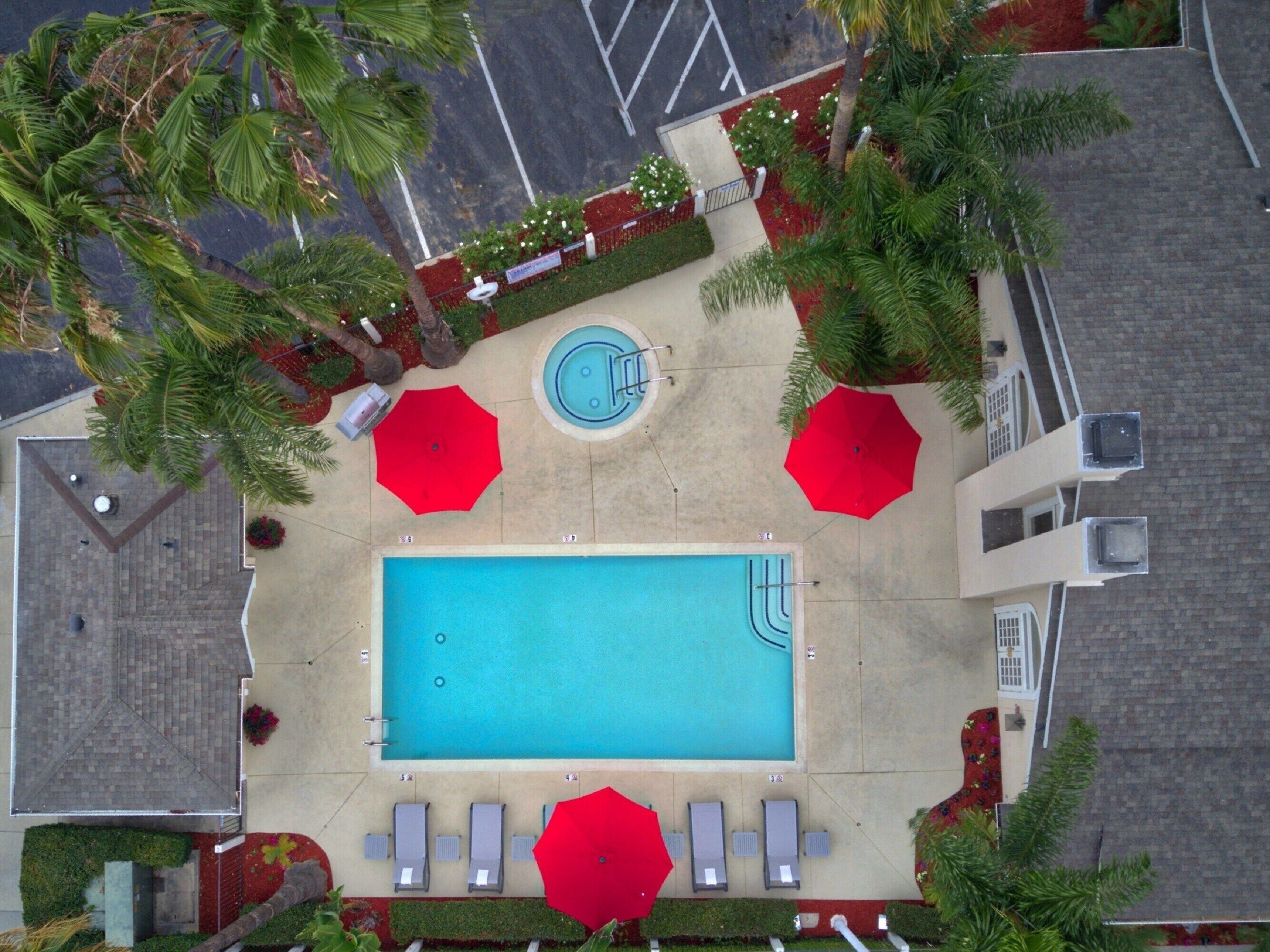 An aerial view of a swimming pool area with a pool, sun loungers, and umbrellas.