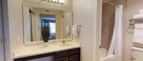 A bathroom with a sink, mirror, towel rack, and shower.