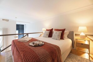 Camera d'albergo con un letto, un comodino con una lampada, un vassoio con asciugamani e una tazza, e vista sull'esterno.