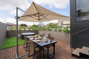 Una terrazza sul tetto con un tavolo apparecchiato per mangiare, una vasca idromassaggio e un grande ombrellone.