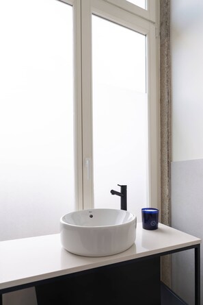 Un lavandino bianco con un rubinetto nero, una tazza blu e una finestra.