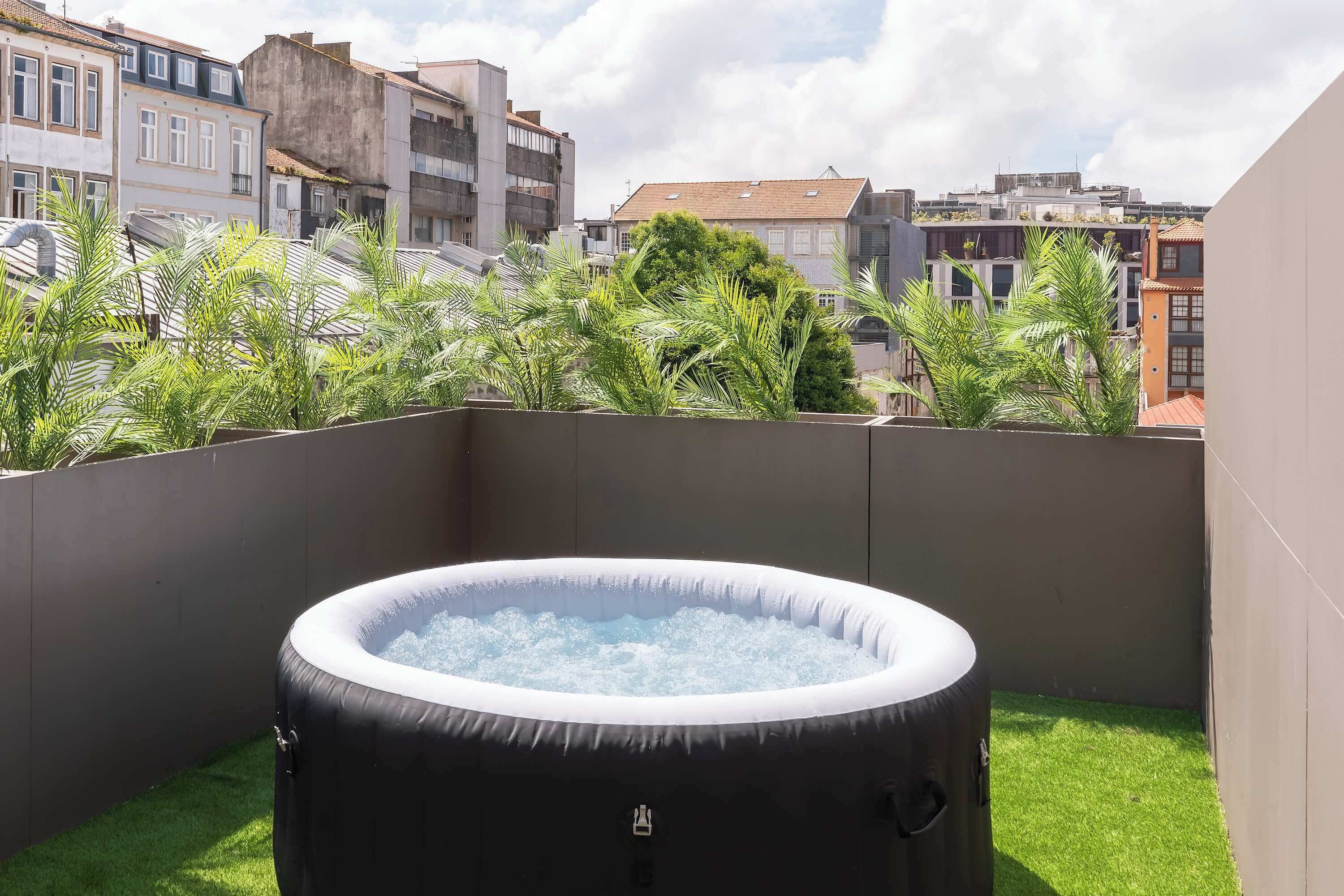 A rooftop with a hot tub surrounded by greenery and buildings in the background.