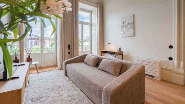 En moderne stue med sofa, lille bord, lampe og et stort vindue med gardiner.
