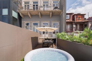 Ein modernes Gebäude mit Balkon, Whirlpool und Terrassenbereich mit Tisch und Sonnenschirm.