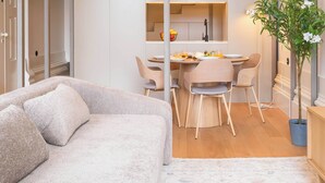En kompakt opholdsstue med sofa, spisebord, stole, en potteplante og en trappe, der forbinder to etager.
