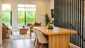 Un salon moderne avec une table à manger en bois, des sièges confortables, de grandes fenêtres et un ventilateur de plafond.