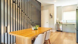 Une cuisine moderne avec des meubles blancs, une table à manger en bois et une porte-fenêtre coulissante.