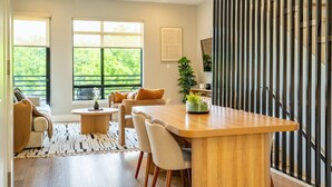 Un salon moderne avec une table à manger en bois, des canapés de couleur beige et une grande fenêtre donnant sur un paysage verdoyant.