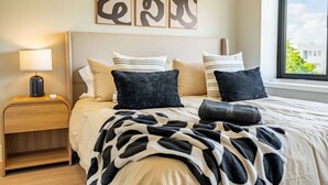 Un lit bien fait, recouvert d’une couverture à motifs, une lampe de chevet et trois œuvres d’art abstraites accrochées au mur.