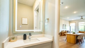 Une salle de bain moderne avec un grand miroir, un lavabo et une petite plante.