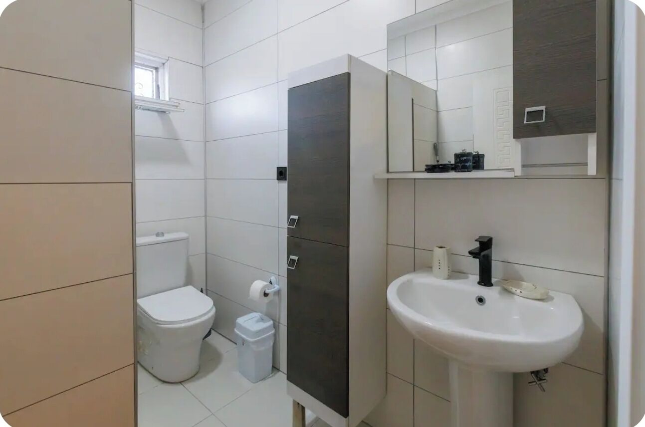 A bathroom with a toilet, a sink, a mirror, and a cabinet.