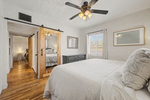 A bedroom with a bed, a ceiling fan, a dresser, a mirror, and a window with blinds. - Midtown Tucson Casita | Near UofA & Dining (Tucson)