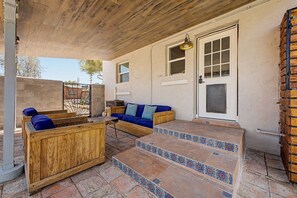 A covered outdoor seating area with wooden furniture, a door with glass panels, and a tiled staircase. - Midtown Tucson Casita | Near UofA & Dining (Tucson)