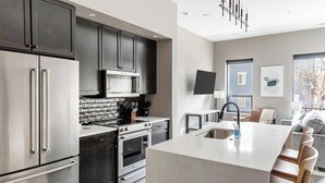 A modern kitchen with stainless steel appliances, a large island, and a dining area with bar stools. - Landing | Stylish 1BD, Yoga Studio, Clubhouse (Columbus)
