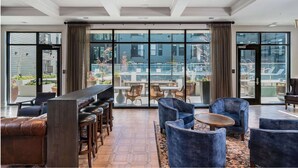 A modern hotel lobby with a bar area, seating, and large windows offering views of the outdoor pool and garden. - Landing | Stylish 1BD, Yoga Studio, Clubhouse (Columbus)