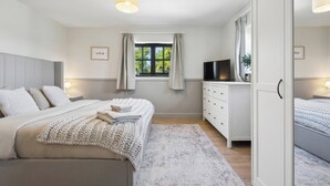 A bedroom with a bed, bedside tables, a TV, a wardrobe, and a window with curtains. - Five Acres Cottage (Rickmansworth)