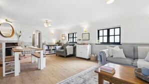 A modern living room with a fireplace, a sofa, a coffee table, and a bookshelf. - Five Acres Cottage (Rickmansworth)