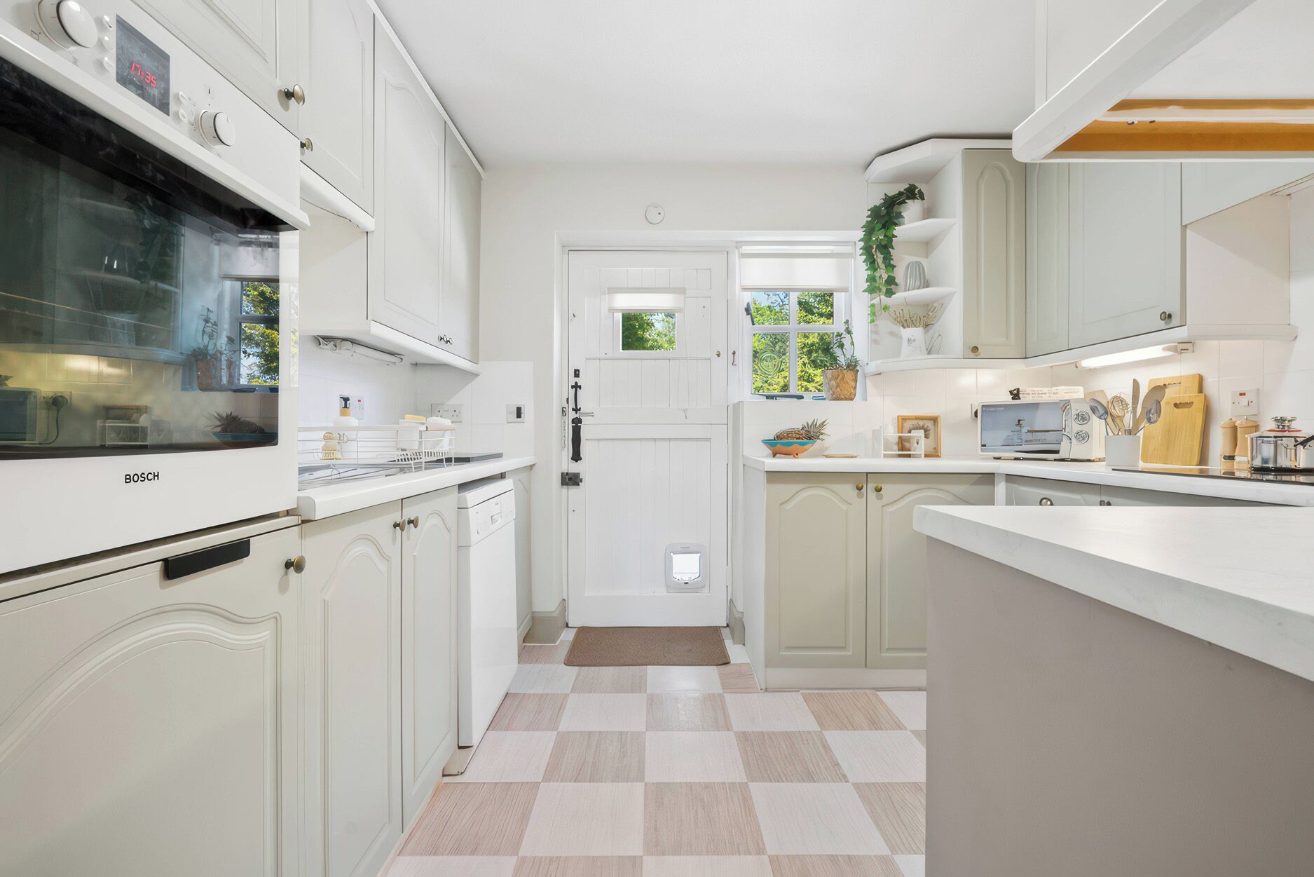 A kitchen with white cabinets, a Bosch oven, a checkered floor, and a window with greenery outside.