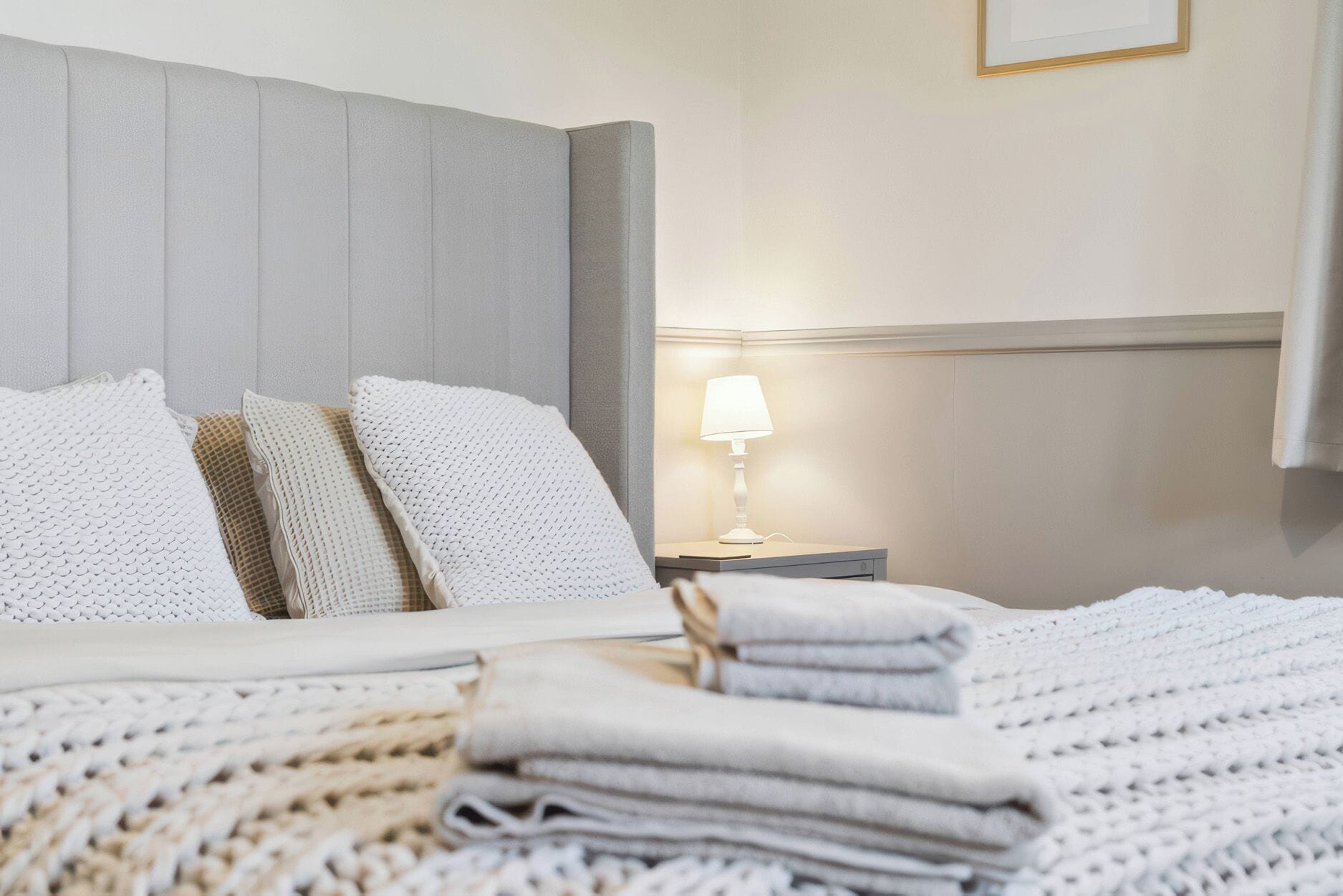A neatly made bed with pillows and a folded blanket, a bedside lamp, and a framed picture on the wall.