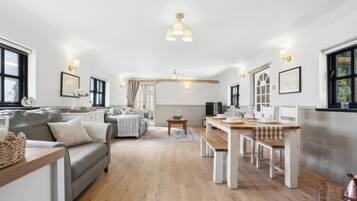 A spacious living area with a sofa, dining table, and a kitchen area in the background.