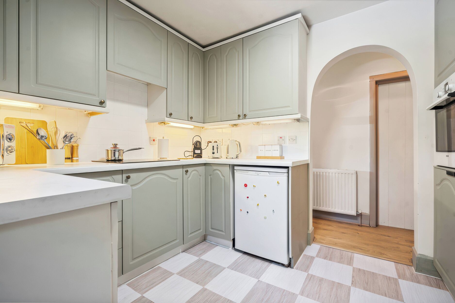 A kitchen with light green cabinets, a white refrigerator, and a checkered floor.
