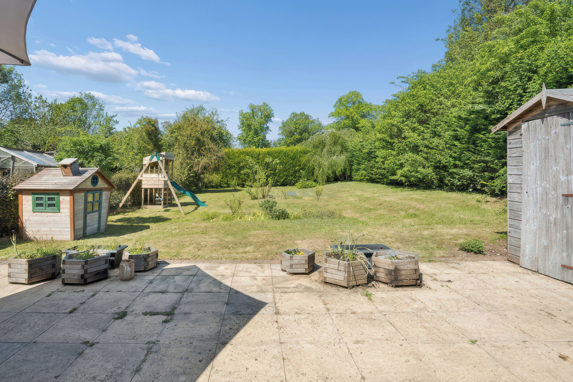 A backyard with a wooden playhouse, a slide, and a shed.