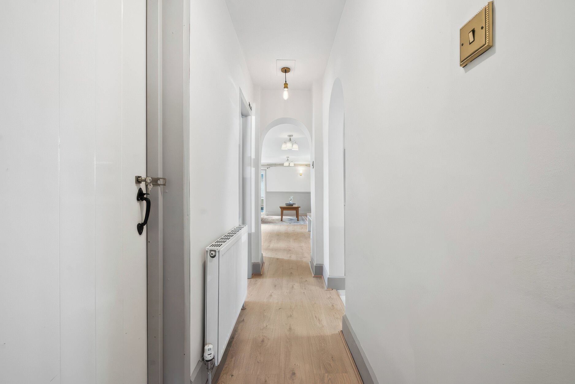 A narrow hallway with white walls, a wooden floor, and a radiator.
