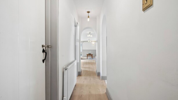 A narrow hallway with white walls, a wooden floor, and a radiator. - Five Acres Cottage (Rickmansworth)
