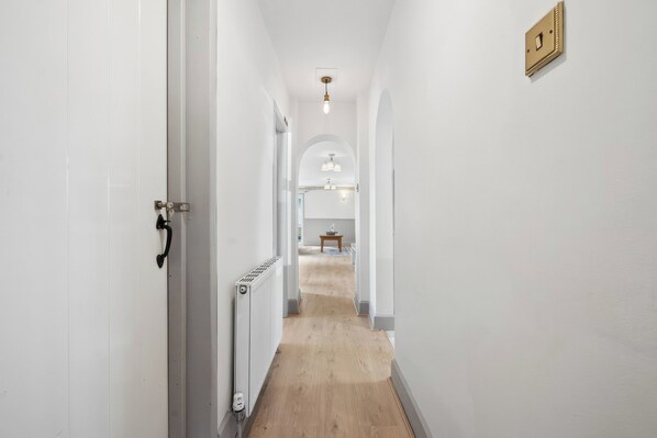A narrow hallway with white walls, a wooden floor, and a radiator.