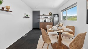 Et moderne køkken med spiseplads, med et stort vindue, mørkt gulv og et spisebord med fletstole.