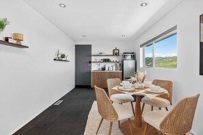 Eine moderne Küche mit Essbereich, ausgestattet mit einem großen Fenster, dunklem Bodenbelag und einem Esstisch mit Korbstühlen.