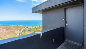 En balkon med udsigt over havet og bakkerne, en dør og et metalgitter.