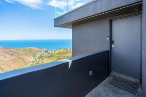 Ein Balkon mit Blick auf das Meer und die Hügel, eine Tür und ein Metallgitter.