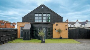 A modern two-story house with a dark exterior, a garage door, and a small front yard with a potted plant. - 6-Bedroom Family Haven with Garden in Aylesbury (Aylesbury)