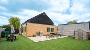 A backyard with a wooden shed, a barbecue grill, a picnic table, and a green lawn. - 6-Bedroom Family Haven with Garden in Aylesbury (Aylesbury)