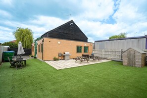 Ein Garten mit einem Holzschuppen, einem Grill, einem Picknicktisch und einem grünen Rasen.