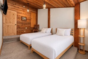 Un dormitorio con dos camas, paredes de madera, una silla, un escritorio y una lámpara.