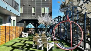Un cortile con prato sintetico, posti a sedere all'aperto e un'area giochi con altalene e scivolo.