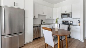 Una cucina moderna con elettrodomestici in acciaio inossidabile, mobili bianchi, un tavolo da pranzo in legno e una piccola pianta in vaso.