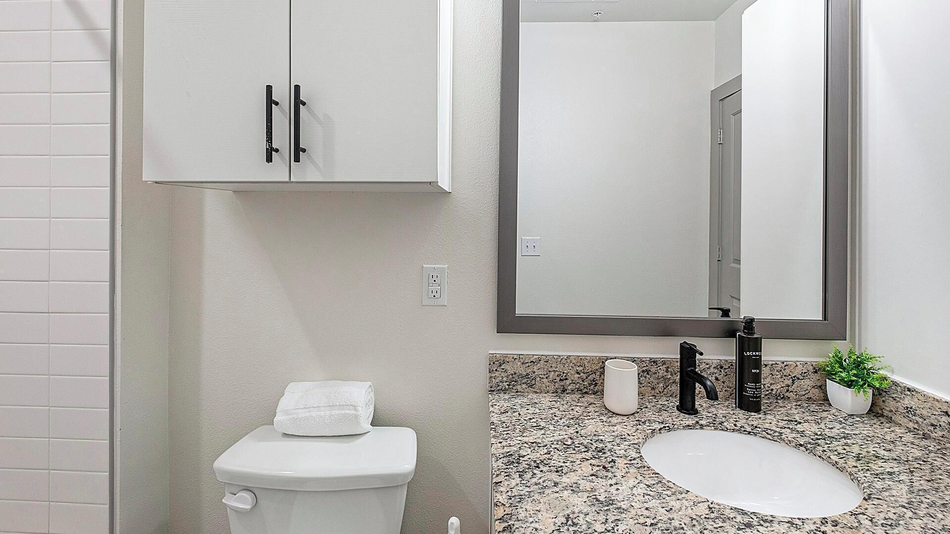 A bathroom with a toilet, a sink, a mirror, and a cabinet.
