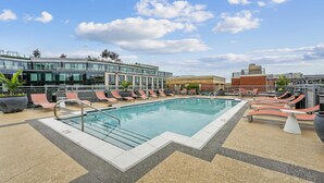 A rooftop pool with lounge chairs, a modern building with glass windows, and a brick structure in the background. - Landing | Stunning 1BD, Courtyard, Gym (Washington)