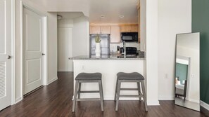 A kitchen with wooden cabinets, a stainless steel refrigerator, a microwave, and two bar stools. - Landing | Incredible 1BD, Courtyard, Gym (Washington)