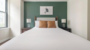 Uma cama bem arrumada com cabeceira, duas mesas de cabeceira com abajures e uma parede verde com um quadro emoldurado.