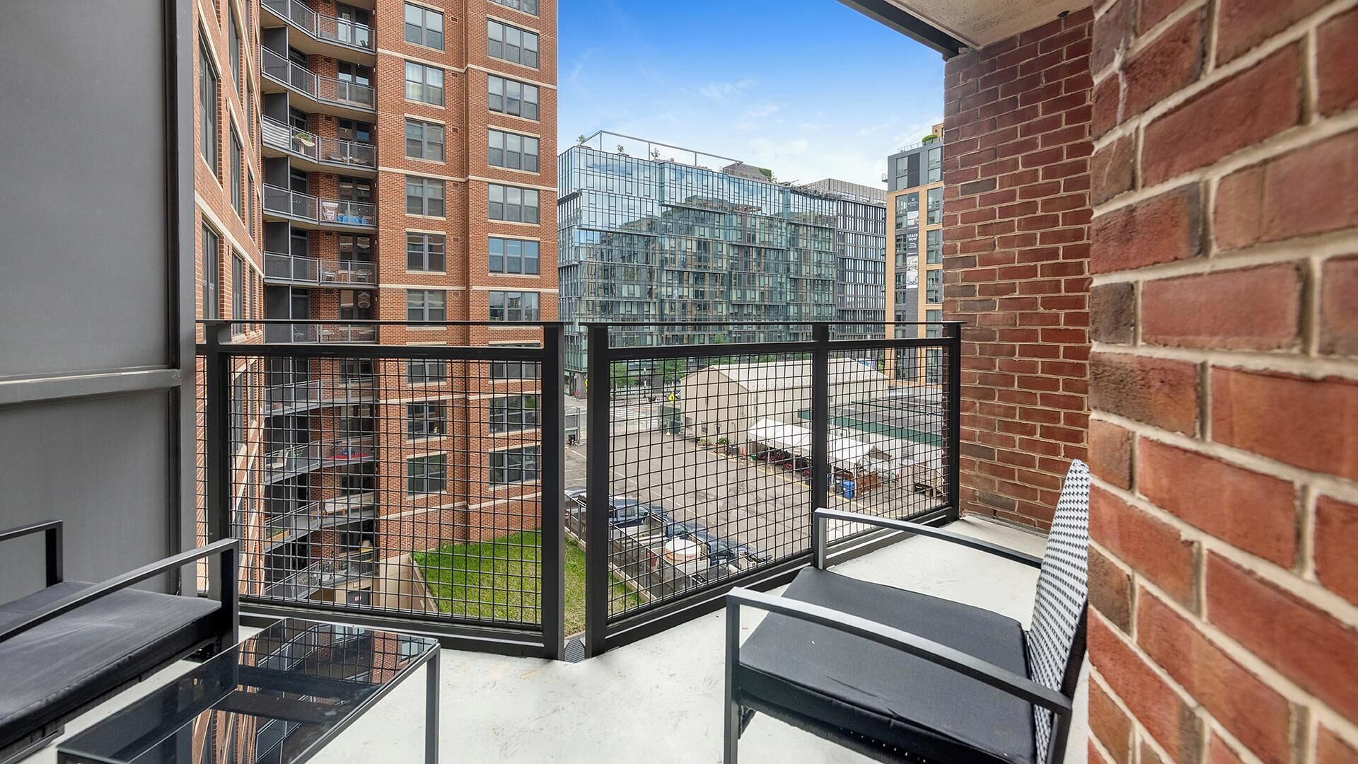 A balcony with a view of high-rise buildings, a metal fence, and a brick wall.
