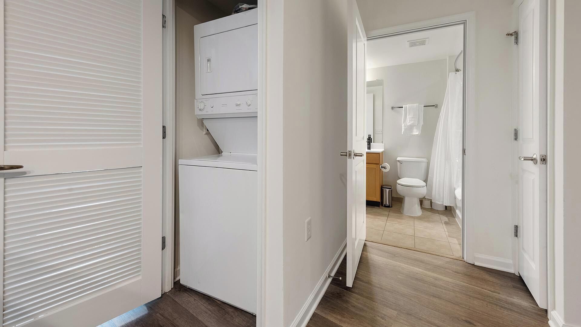 A hallway leading to a bathroom with a toilet, shower, and a laundry area with a washing machine.